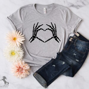 May include: A gray t-shirt with a black skeleton hand design making a heart shape.