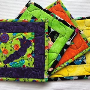 May include: Set of four colorful quilted pot holders with a black background and a variety of designs. The designs include a caterpillar, a cocktail, and a bee.