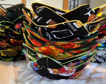 May include: A stack of colorful fabric bowls with various patterns and designs. The bowls are made of quilted fabric and have a yellow trim. The bowls are stacked in a pyramid shape.