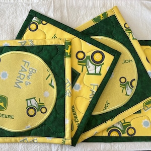 May include: Four green and yellow quilted placemats with a tractor and "Born to Farm" text. The placemats have a green border and a yellow center with a white circle in the center of one placemat.