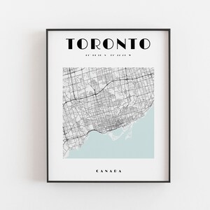 May include: A framed print featuring a detailed map of Toronto, Canada, in black and white, with a light blue section representing Lake Ontario. The city name is displayed in bold, black letters at the top.