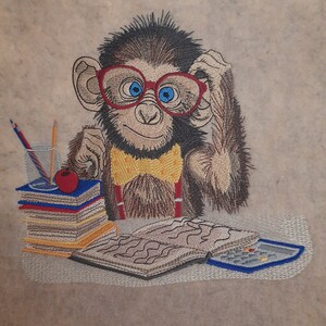 May include: Embroidered image of a monkey wearing red glasses, a yellow bow tie, and suspenders. The monkey is sitting at a desk with books, pencils, and an apple. A calculator and open book are also on the desk.