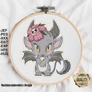 Könnte beinhalten: Ein Stickrahmen mit einem Cartoon-Drachen-Design. Der Drache ist grau mit gelben Augen, grauen Flügeln und einer rosa Blume auf dem Kopf. Der Text "Machineembroidery Design" befindet sich unten. Der Text "-JEF -PES -XXX -DST -EXP -VP3 -HUS" ist ebenfalls enthalten.