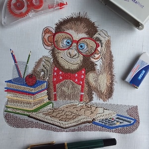 Pode incluir: Desenho bordado de um macaco usando óculos vermelhos, gravata borboleta vermelha e suspensórios. O macaco está sentado em uma mesa com uma pilha de livros, uma maçã e uma calculadora.