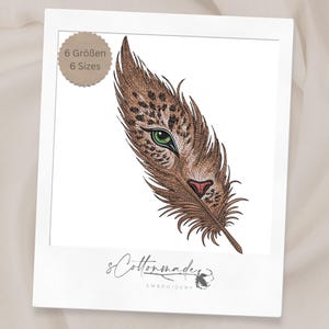 Puede incluir: Un diseño de bordado que presenta una pluma marrón con manchas de leopardo, un ojo verde y una nariz rosa. Una insignia circular en la esquina superior izquierda muestra el texto 6 Größen 6 Sizes. El centro inferior incluye el texto sCottonmade EMBROIDERY.