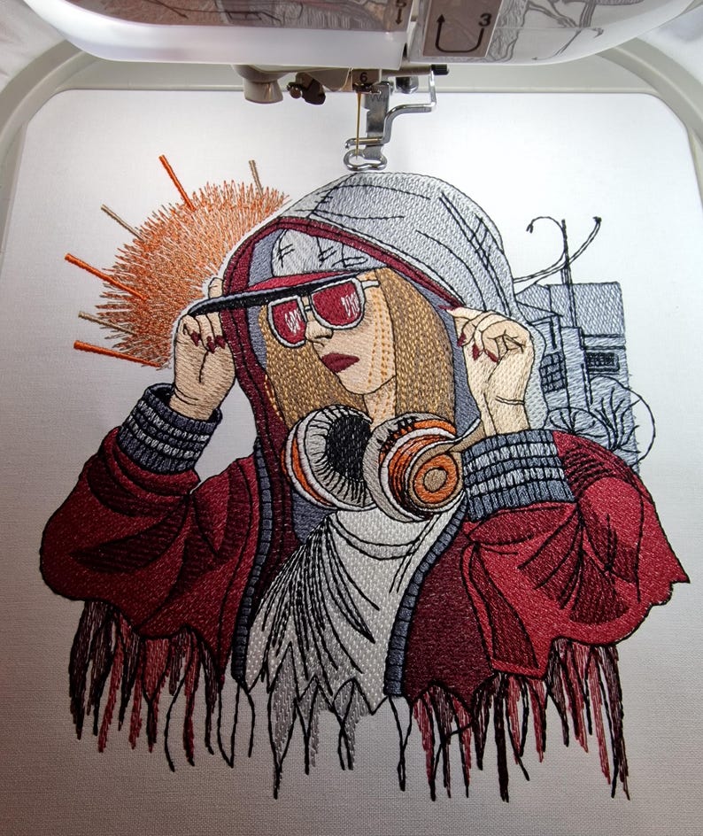 Op de afbeelding: Geborduurd kunstwerk van een persoon met een rode hoodie, zonnebril en koptelefoon. Het ontwerp toont een zonsopgang en een stadsgezicht. De borduurwerk is gedetailleerd met verschillende kleuren en texturen.