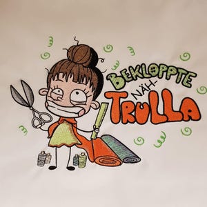 Könnte beinhalten: Gesticktes Design mit einer Cartoonfigur, die eine Schere, Stoff und Garnrollen hält. Der Text "BEKLOPPTE NÄH-TROLLA" ist in Orange und Grün gehalten. Die Figur hat braune Haare und trägt ein gelb-oranges Outfit. Grüne Wirbel umgeben die Figur.