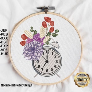 May include: Machine embroidery design of a vintage alarm clock with a bouquet of flowers in shades of purple, red, and white. The design includes the text "Machineembroidery Design".