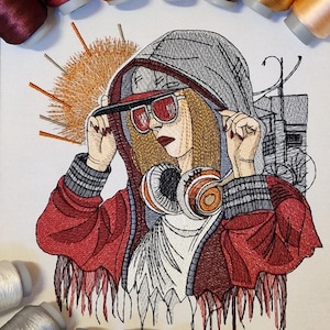 Op de afbeelding: Geborduurd kunstwerk met een persoon in een rode jas, grijze hoodie en zonnebril, met een koptelefoon. Het kunstwerk is omgeven door spoelen kleurrijk garen, wat duidt op een knutselproject. De stijl is gedetailleerd.