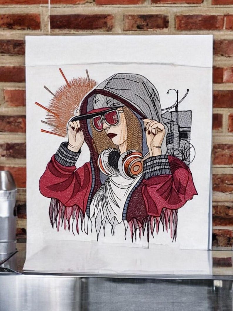 Op de afbeelding: Geborduurd kunstwerk van een persoon met een rode jas, grijze hoodie en zonnebril, met een koptelefoon. Het kunstwerk heeft een streetstyle thema, met een stadsgezicht op de achtergrond en een zonnester ontwerp.