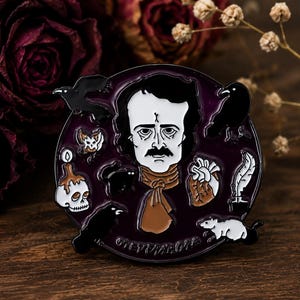 May include: A round enamel pin featuring a central portrait of Edgar Allan Poe surrounded by gothic motifs including two black ravens, a skull with a melting candle, a black cat, a human heart, a white rat, and a quill pen on a dark purple background.