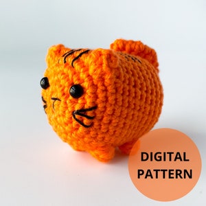 Puede incluir: Juguete de peluche de gato naranja tejido a crochet con ojos negros y bigotes. El texto DIGITAL PATTERN es visible en la esquina inferior derecha de la imagen.