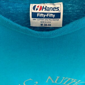 May include: A turquoise blue t-shirt with a white graphic that says "Young Authors" with a heart and arrow. The shirt has a Hanes Fifty-Fifty tag with the size M 38-40.