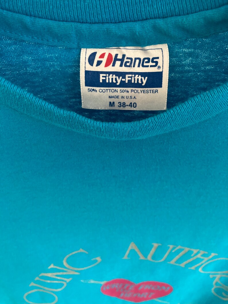 May include: A turquoise blue t-shirt with a white graphic that says "Young Authors" with a heart and arrow. The shirt has a Hanes Fifty-Fifty tag with the size M 38-40.