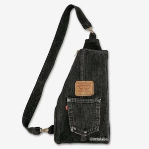 May include: A black denim crossbody bag with a zipper closure and a Levi's patch on the front. The bag has a distressed look and a small pocket on the front. The bag is worn over the shoulder.