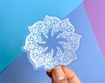 Könnte beinhalten: Weißer Blumen-Mandala-Aufkleber auf blauem und violettem Hintergrund. Der Aufkleber ist transparent und hat ein weißes Design.