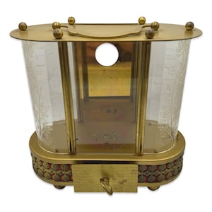 May include: An antique brass and glass display case with a key lock. The case has a gold-colored frame, clear glass sides with etched floral patterns, and a red and gold decorative base. The top features small gold spheres.