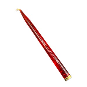 May include: A single red taper candle with a gold-colored tip and base. The candle is a deep red color with flecks of red throughout. The candle is set against a white background.
