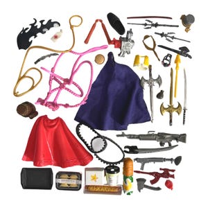 May include: A selection of toy accessories, including a red cape, a purple cape, swords, guns, a pink whip, and miniature food items. Other items include a black flame, a medical cross, and a gold-coloured ring.