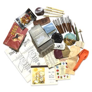 Könnte beinhalten: Eine Sammlung von Vintage-Artikeln, darunter ein Hunde-Buch, ein Dirt Devil-Anleitungsblatt, eine Metallbox, mehrere Werkzeuge mit Holzgriffen, ein kleiner blauer Beutel, eine bemalte runde Scheibe, eine Kalorienzähler-Karte und orangefarbene Messlöffel.
