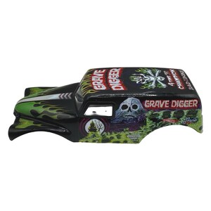 Pu&ograve; includere: Carrozzeria di camion giocattolo nera con fiamme verdi e le parole "Grave Digger" e "4 Time Champion" in bianco e rosso. Una grafica a teschio &egrave; sul lato. Il giocattolo &egrave; un veicolo Hot Wheels Monster Jam.