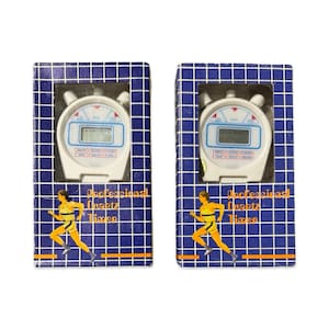 Op de afbeelding: Twee witte quartz timers in blauwe dozen met een rasterpatroon. Elke timer heeft een digitale display en rode, witte en blauwe accenten. De dozen hebben een hardloper grafiek en de tekst "Professional Quartz Timer."