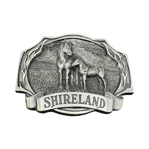 May include: Silver-toned metal belt buckle with a detailed relief of two horses in a field. The word "SHIRELAND" is displayed on a banner across the bottom. The buckle has an ornate, decorative border.
