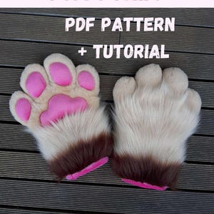 May include: A pair of fluffy paw gloves with pink pads and brown cuffs. The text "PUFFY PAWS PDF PATTERN + TUTORIAL" is displayed in pink and white above the gloves. The gloves are on a wooden surface.