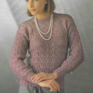 May include: A mauve knitted sweater with a delicate lace pattern. The sweater has long sleeves and a round neckline. The model is wearing a pearl necklace.