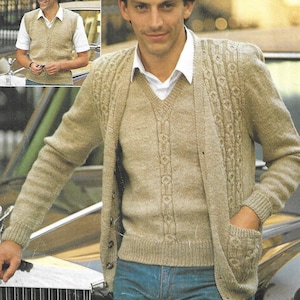 May include: A man wearing a beige knitted cardigan with a matching V-neck sweater and a white collared shirt underneath. The cardigan has a button closure and pockets. The sweater has a decorative pattern down the front. The man is also wearing blue jeans.