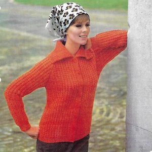 Op de afbeelding: Een vrouw draagt een rode gebreide trui met een wit en bruin luipaardprint hoofddoek. De trui heeft een kraag en lange mouwen. De vrouw leunt tegen een betonnen muur. De tekst "Patons Ariel Triple Knitting" en "Three sizes to fit 34-38 inch bust" is zichtbaar bovenaan de afbeelding.