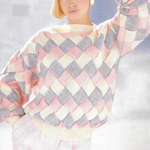 Puede incluir: Un suéter de punto con un patrón geométrico en rosa, blanco y gris. El suéter tiene cuello redondo y mangas largas. La modelo lleva el suéter con pantalones rosas.