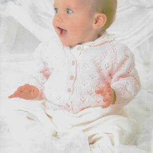 May include: A white knitted baby cardigan with a button closure and a delicate lace pattern. The cardigan is made with Patons Fairytale 4 Ply yarn and is sized for a baby 14-20 inches (36-51 cm).