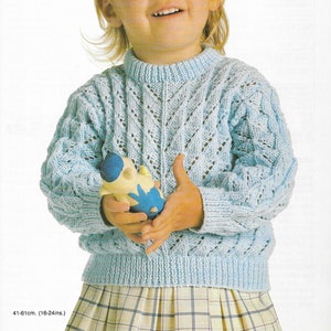 May include: A light blue knitted jumper with a lacy pattern. The jumper is worn by a young child holding a toy. The pattern is called "Peter Pan" and is a 4 ply yarn. The code for the pattern is P539.