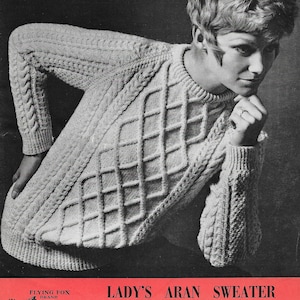 May include: A black and white photo of a woman wearing a white aran knit sweater. The sweater has a cable knit pattern. The photo is from a vintage knitting pattern leaflet. The text on the leaflet reads "Lady's Aran Sweater 100% Pure Wool Garryowen For Aran Knitting 6d."