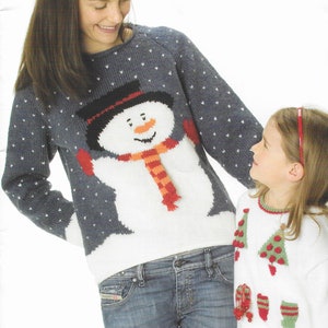 Pu&ograve; includere: Due persone indossano maglioni di lana a tema natalizio. L'adulto indossa un maglione blu con un disegno di pupazzo di neve bianco. Il bambino indossa un maglione bianco con un disegno di albero di Natale verde. DESIGN 5 & 6 ARAN & DK