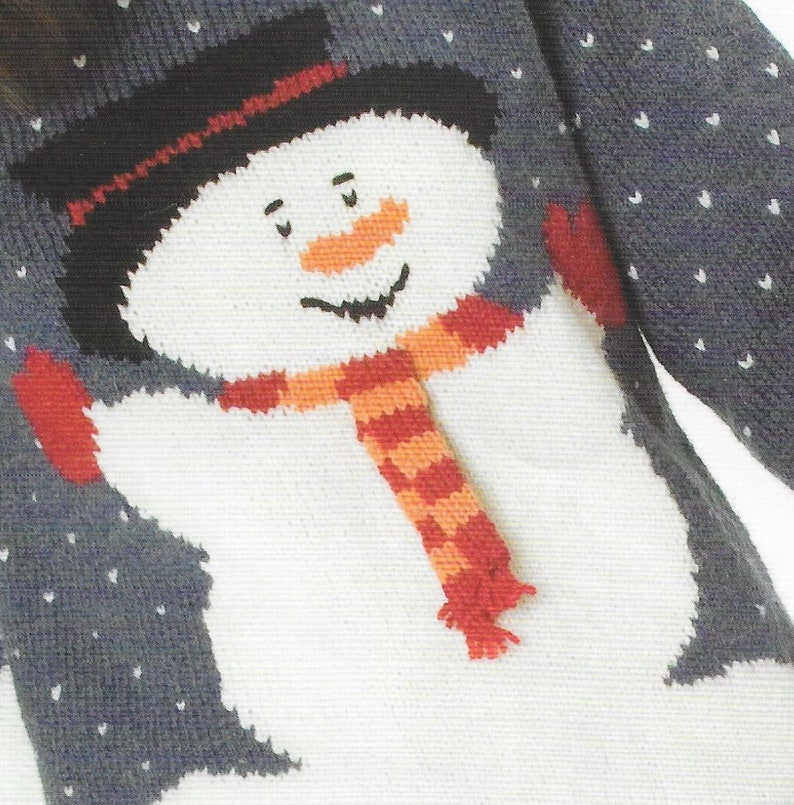 Pu&ograve; includere: Un maglione di lana bianco con un disegno di pupazzo di neve. Il pupazzo di neve indossa un cappello nero, una sciarpa rosso e arancione e guanti rossi. Il maglione ha uno sfondo grigio con pois bianchi.