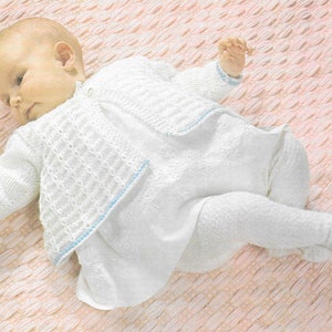 Op de afbeelding: Een wit gebreid babyvest met een blauwe rand, gedragen door een baby die op een roze deken ligt.