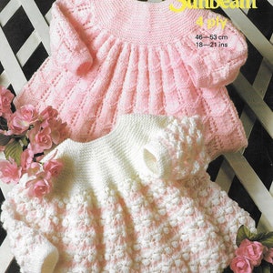 May include: Two knitted baby dresses, one pink and one white with pink accents. The dresses are made with a 4-ply yarn and are sized for 18-21 inches.