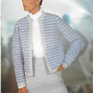 Puede incluir: Un cárdigan de punto de ganchillo azul claro y blanco con una falda a juego. El cárdigan tiene un patrón de cuadros y la falda es de un solo color.