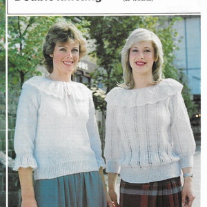Può includere: Due donne indossano maglioni di lana bianca con un colletto a volant. I maglioni hanno un motivo a pizzo. La donna a sinistra indossa una gonna blu. La donna a destra indossa una gonna a quadri rossi e neri. L'immagine include il testo "Double knitting" e "Sizes 81-102 cms (32-40 inches)" e il numero "477".