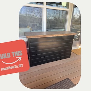 Può includere: Un bar in legno nero con un piano in legno, su un ponte in legno. Il bar ha un design a doghe orizzontali. Il testo "BUILD THIS" e "LearnHowTo.DIY" è su uno sfondo rosso.