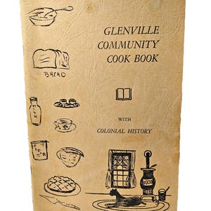 May include: A tan, textured softcover book titled GLENVILLE COMMUNITY COOK BOOK WITH COLONIAL HISTORY. The cover features black line drawings of kitchen items including bread, a milk bottle, a pie, a stove, and a cat on a rug.