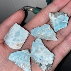 May include: Five pieces of blue and white larimar rough stones. The stones are various shapes and sizes.