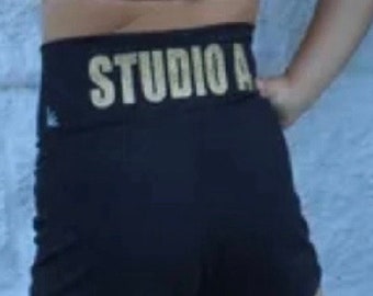 Op de afbeelding: Zwarte shorts met een gouden "STUDIO A" tailleband.