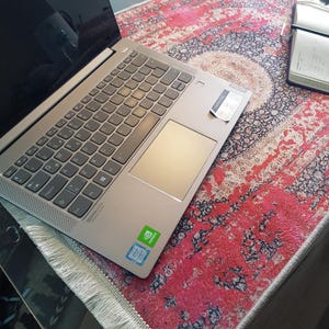 Może przedstawiać: Srebrny laptop Lenovo z szarą klawiaturą i gładzikiem. Laptop ma naklejkę z logo Intel Core i7 i NVIDIA. Laptop leży na czerwono-czarnym wzorzystym dywanie.