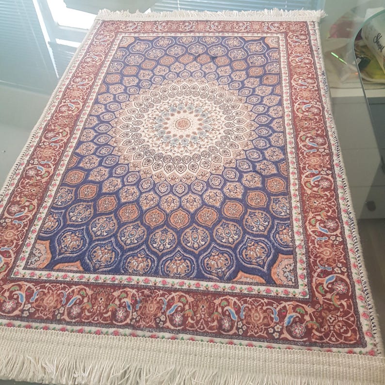 May include: A rectangular rug with a detailed floral pattern in shades of blue, orange, and cream. The rug has a central medallion design and a border with intricate floral motifs. The edges are finished with a white fringe.