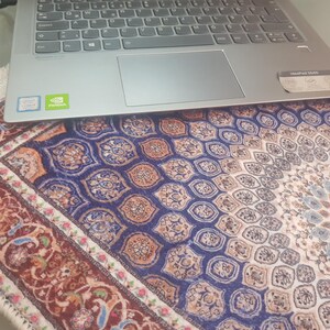 May include: A silver laptop rests on a patterned rug. The rug features a repeating design in shades of blue, orange, and white, with a detailed border in red and cream. The laptop has a keyboard, touchpad, and the Intel Core i5 and NVIDIA logos.