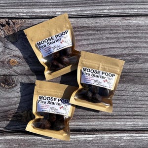 Peut inclure: Trois petits sacs en papier brun avec des fenêtres en plastique transparent contenant des allume-feu brun foncé étiquetés "Moose Poop Fire Starter".
