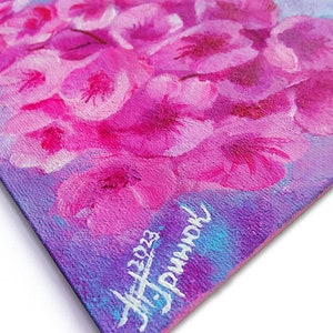 Puede incluir: Un primer plano de una pintura de flores rosas sobre un fondo morado. La pintura est&aacute; firmada "JF 2023" y "remarkable" en pintura blanca.